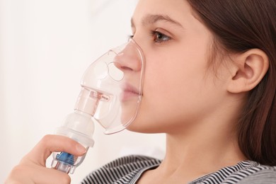Photo of Cute girl using nebulizer for inhalation on white background, closeup