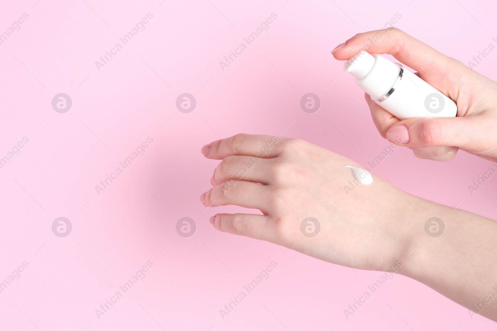 Photo of Woman applying cream on her hand against pink background, closeup. Space for text