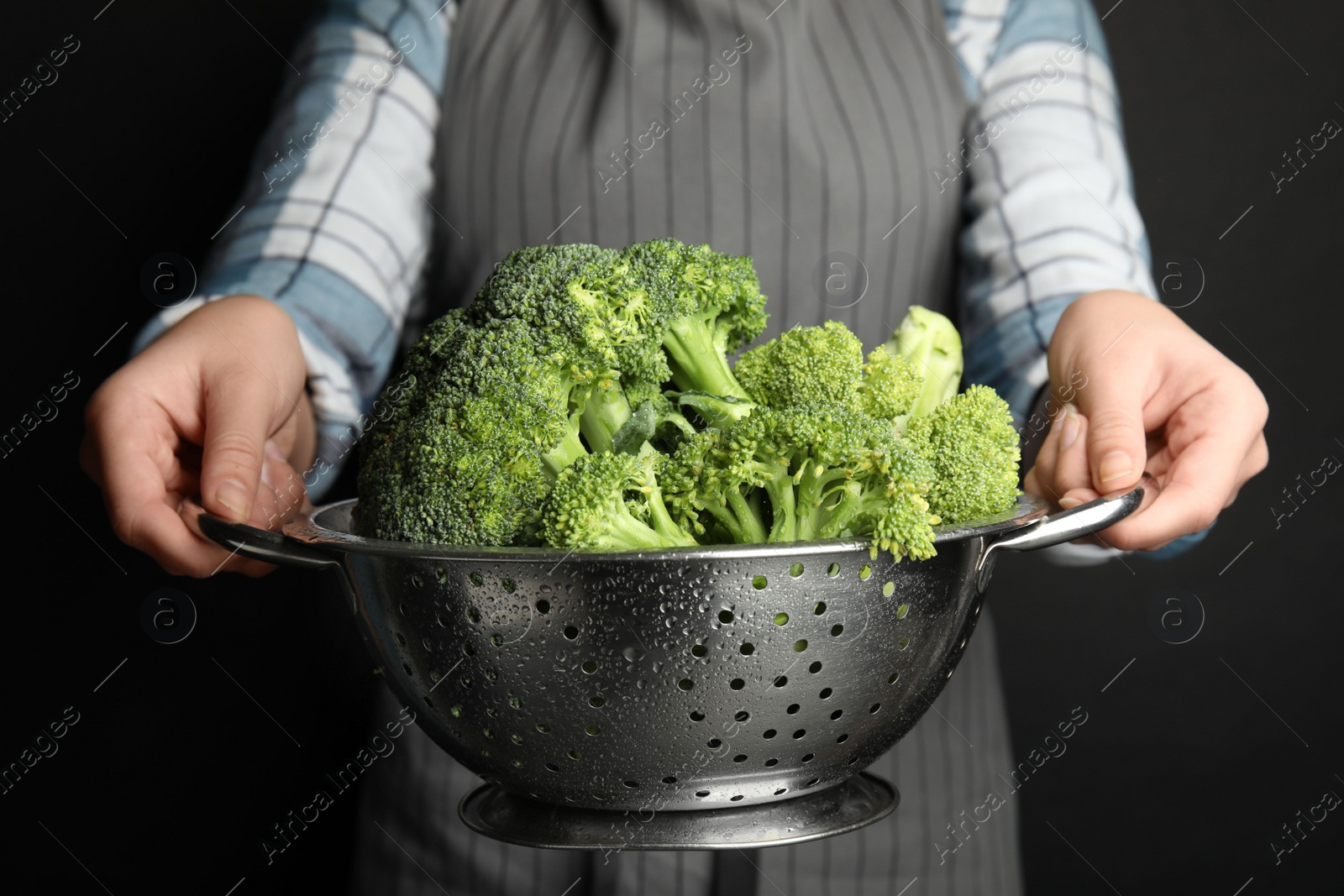 Photo of Woman holding colander with fresh green broccoli on black background, closeup