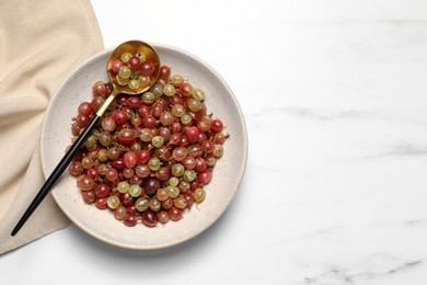 Plate of fresh ripe gooseberries and spoon on white marble table, top view. Space for text