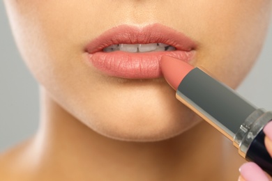 Young woman applying lipstick on color background, closeup