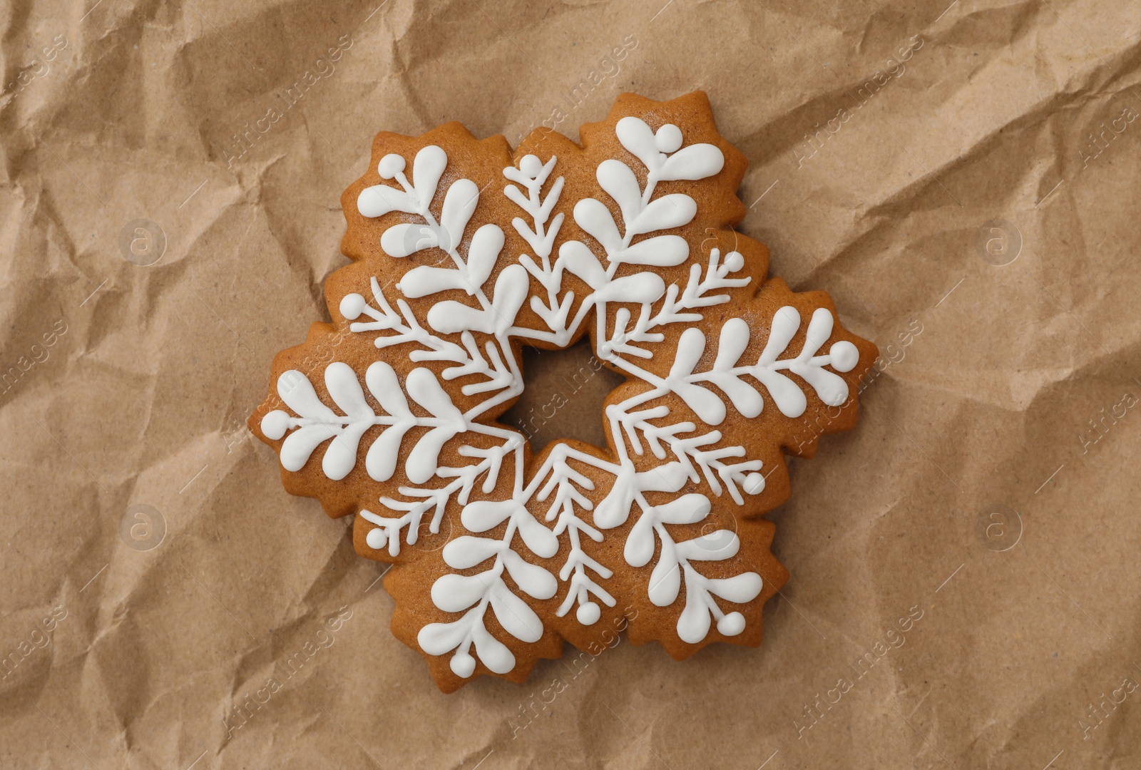 Photo of Christmas snowflake shaped gingerbread cookie on crumpled parchment, top view