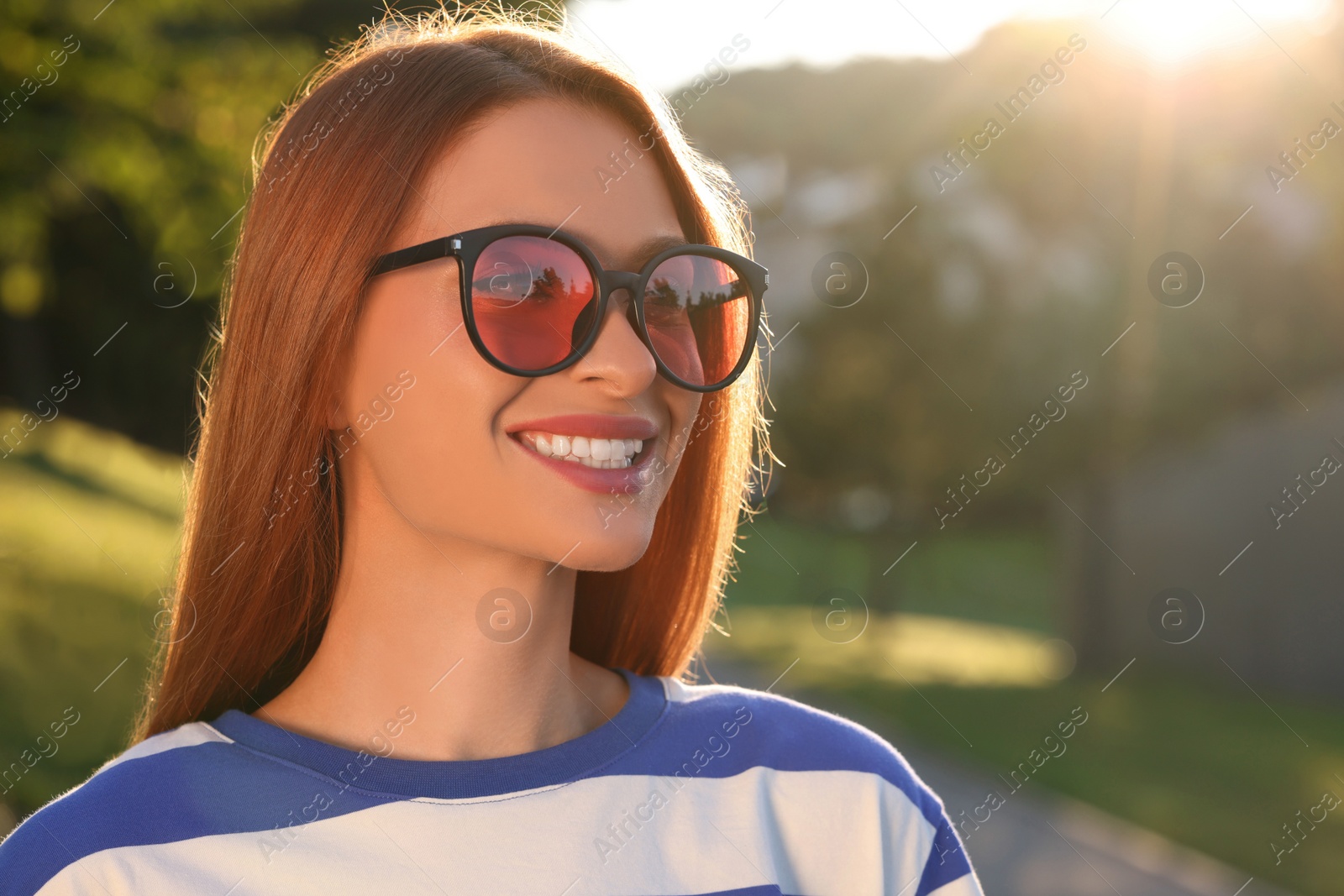 Photo of Beautiful smiling woman wearing sunglasses in park, space for text