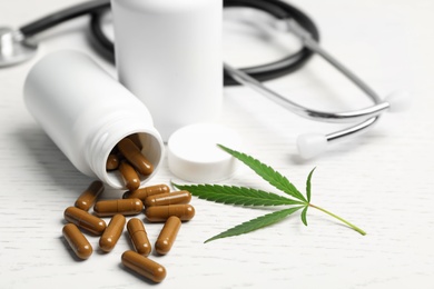 Photo of Hemp leaf, bottles with capsules and stethoscope on white wooden table