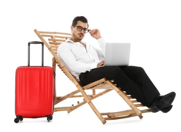 Photo of Young businessman with laptop and suitcase on sun lounger against white background. Beach accessories
