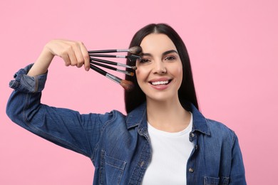 Photo of Happy woman with different makeup brushes on pink background