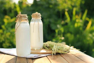 Photo of Bottles of tasty fresh milk on wooden table outdoors, space for text