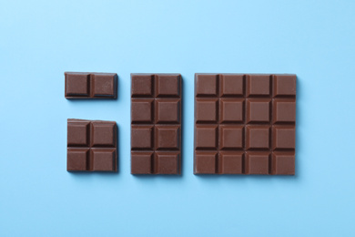 Photo of Tasty milk chocolate on light blue background, flat lay