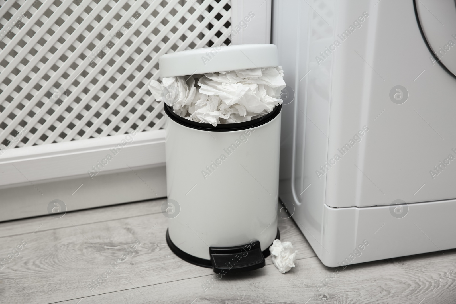 Photo of Used paper tissues in trash can near washing machine indoors