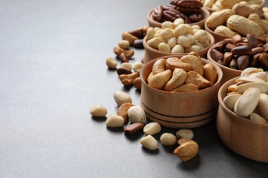Photo of Bowls with organic nuts on grey background, space for text. Snack mix