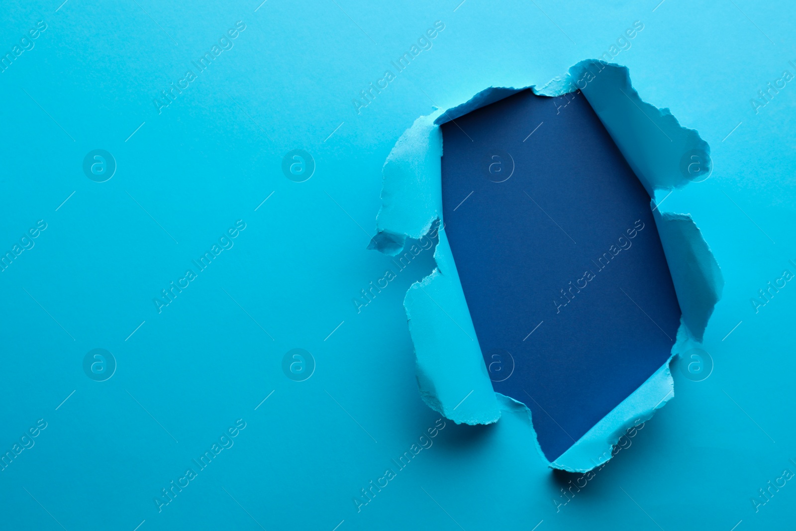 Photo of Hole in light blue paper on color background, space for text