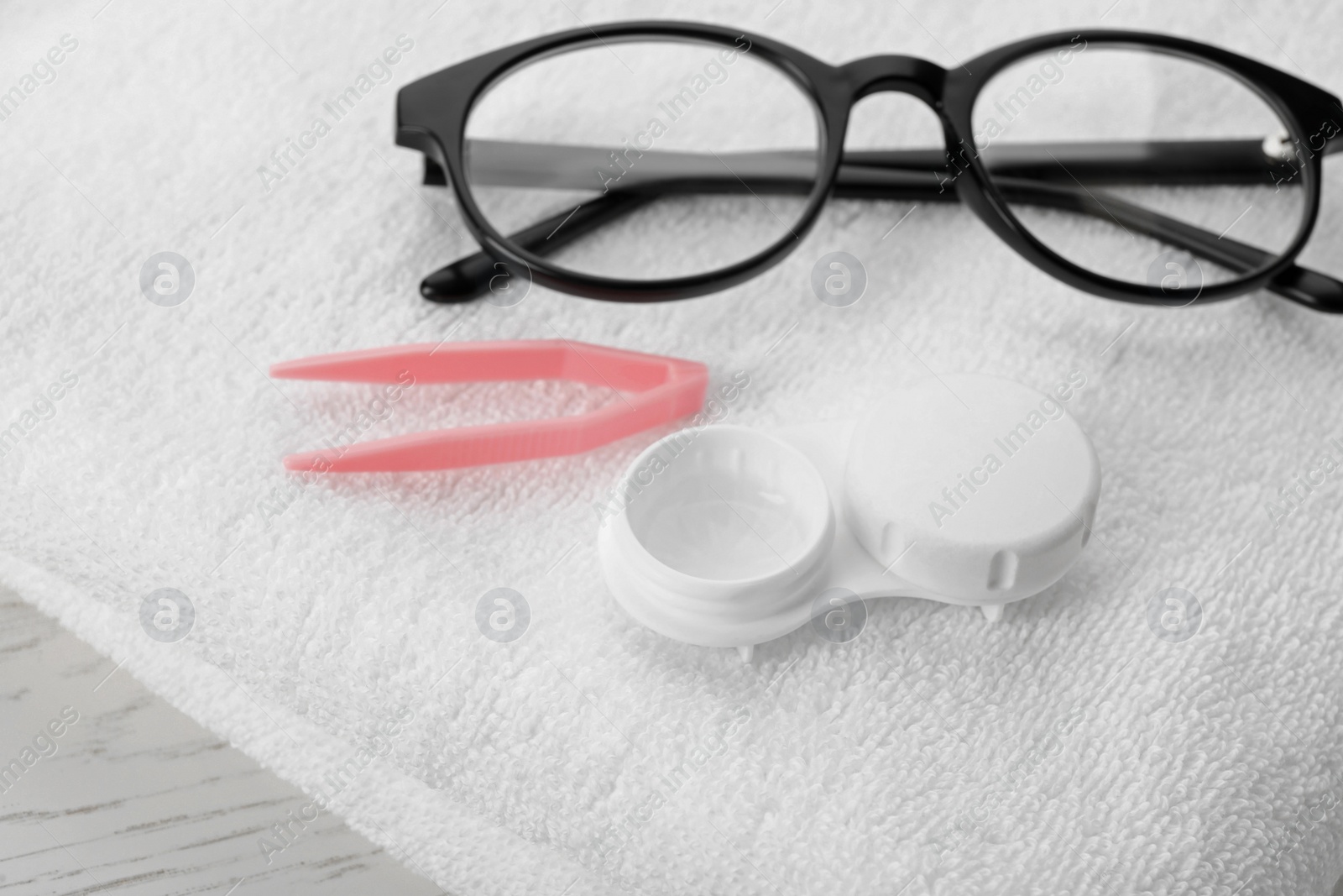 Photo of Case with contact lenses, tweezers, glasses and towel on white table, closeup