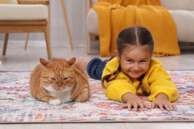Photo of Happy little girl and cute ginger cat on carpet at home
