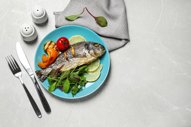 Photo of Delicious roasted fish with lemon and vegetables on grey marble table, flat lay. Space for text