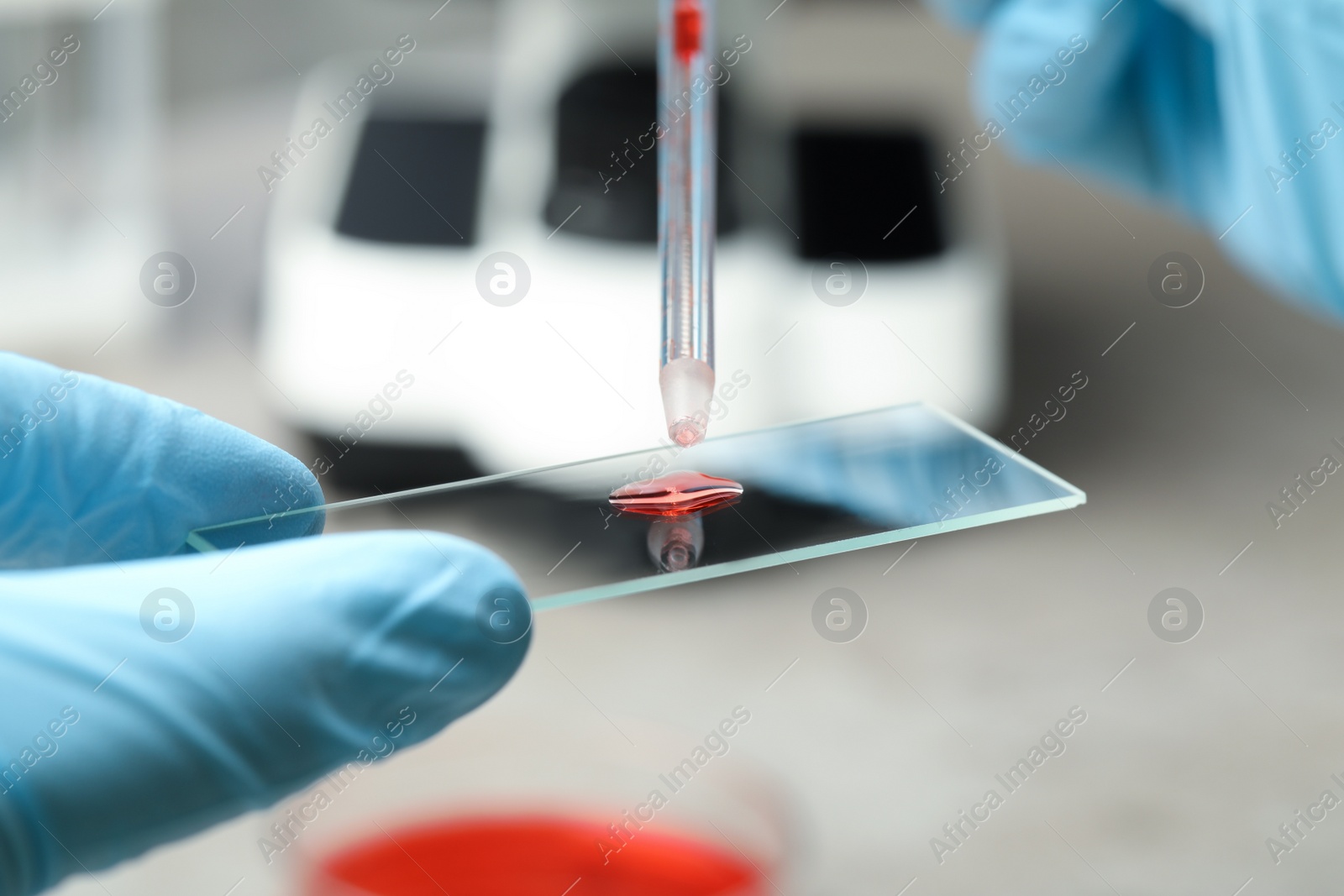 Photo of Scientist dripping sample of red liquid onto microscope slide in laboratory, closeup