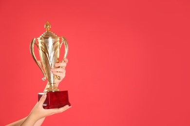 Photo of Child holding golden winning cup on red background, closeup. Space for text