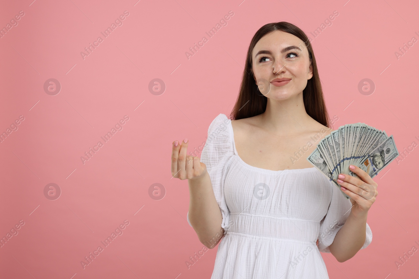 Photo of Woman with dollar banknotes showing money gesture on pink background, space for text