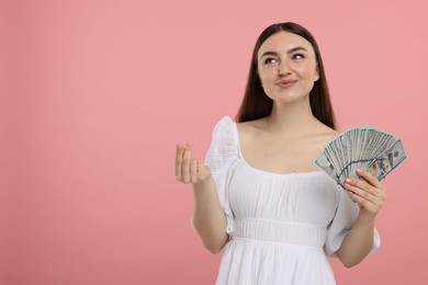 Woman with dollar banknotes showing money gesture on pink background, space for text