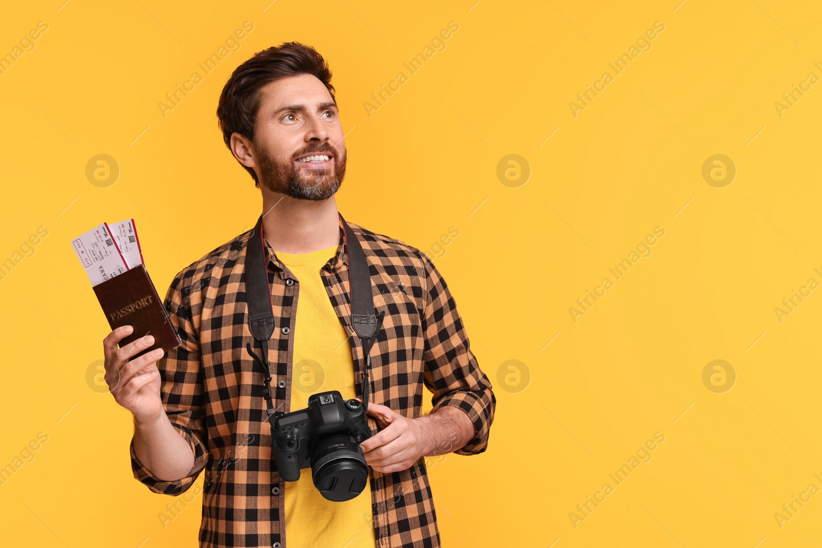 Photo of Smiling man with passport, tickets and camera on yellow background. Space for text