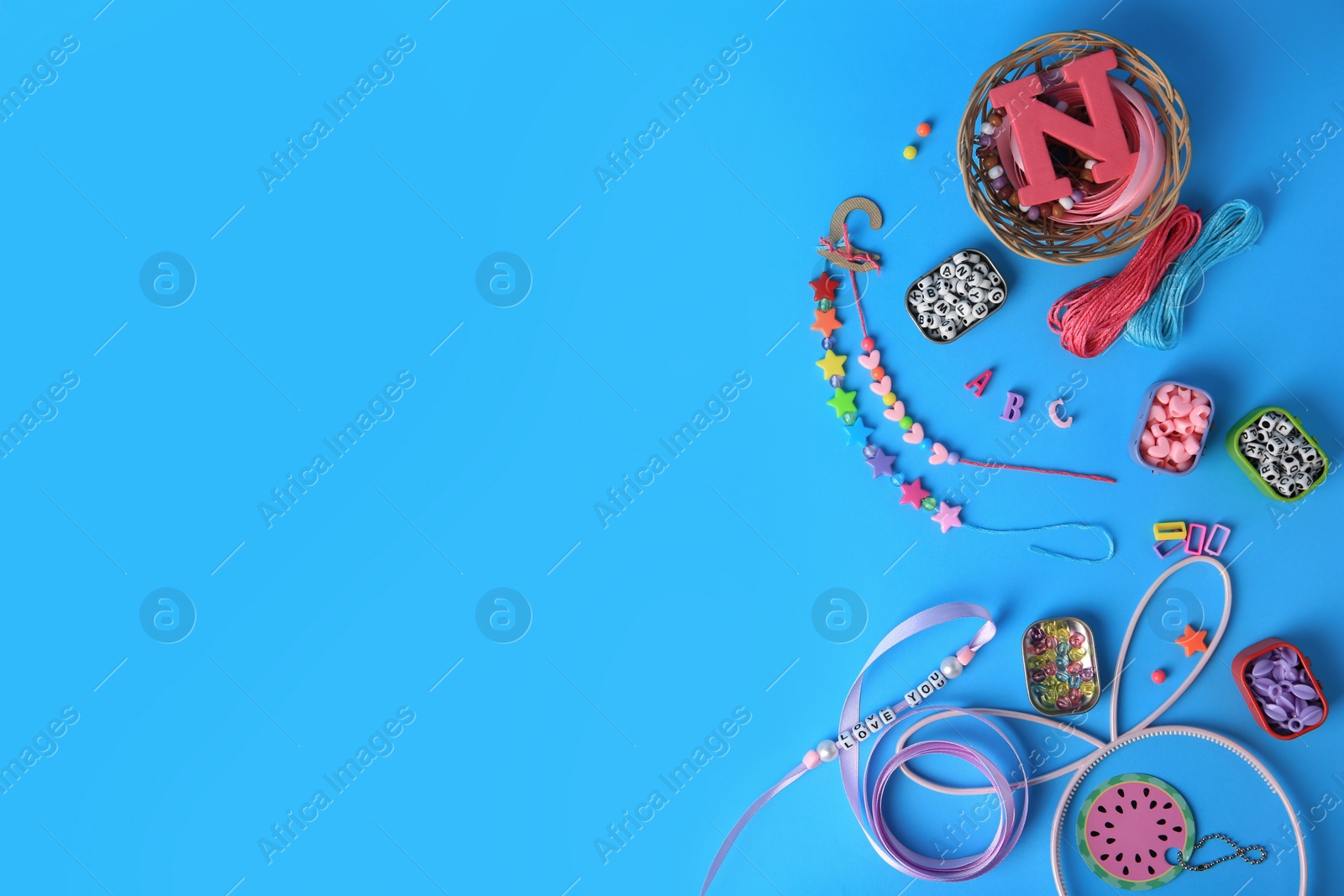 Photo of Kid`s handmade jewelry kit. Colorful beads, ribbon and bracelets on light blue background, flat lay. Space for text