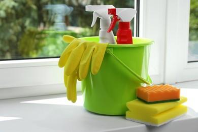 Photo of Green bucket with cleaning supplies and tools on window sill indoors