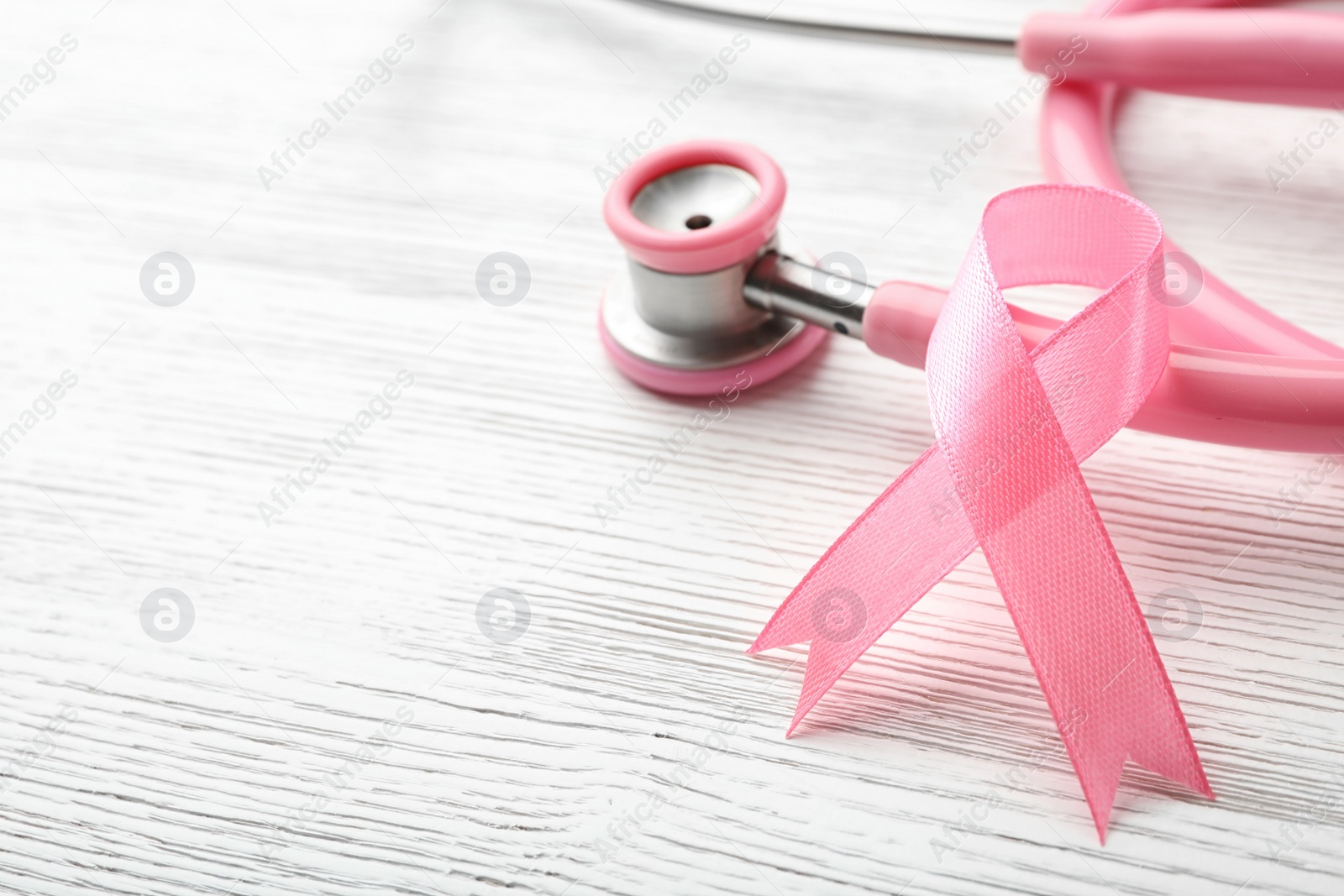 Photo of Pink ribbon and stethoscope on wooden background, space for text. Breast cancer concept