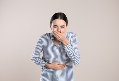 Woman suffering from stomach ache and nausea on beige background. Food poisoning