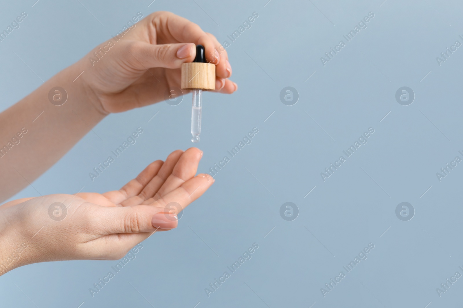 Photo of Woman dripping serum from pipette on her hand against light grey background, closeup. Space for text