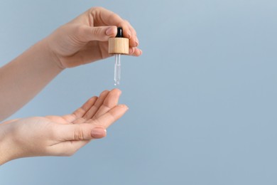 Photo of Woman dripping serum from pipette on her hand against light grey background, closeup. Space for text