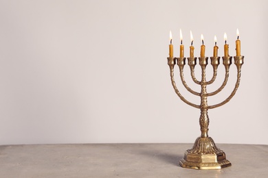 Photo of Golden menorah with burning candles on table against light grey background, space for text