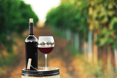 Photo of Bottle and glass of red wine on wooden barrel in vineyard