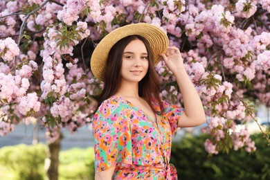 Photo of Beautiful woman in straw hat near blossoming tree on spring day