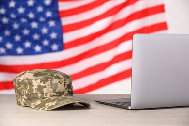 Photo of Cap and laptop on wooden table against flag of USA. Military education