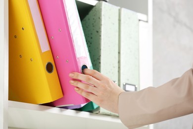 Photo of Woman taking folder with documents from shelf in office, closeup