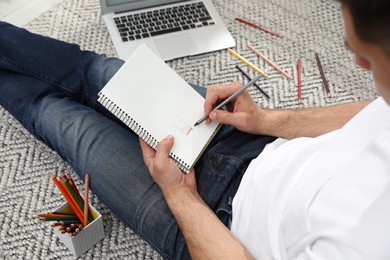 Photo of Man drawing in notebook at online lesson on floor, closeup. Distance learning