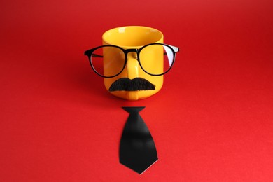 Man's face made of cup, fake mustache, glasses and paper tie on red background