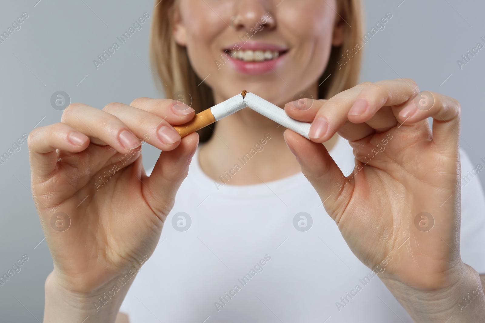 Photo of Stop smoking concept. Woman breaking cigarette on light grey background, closeup