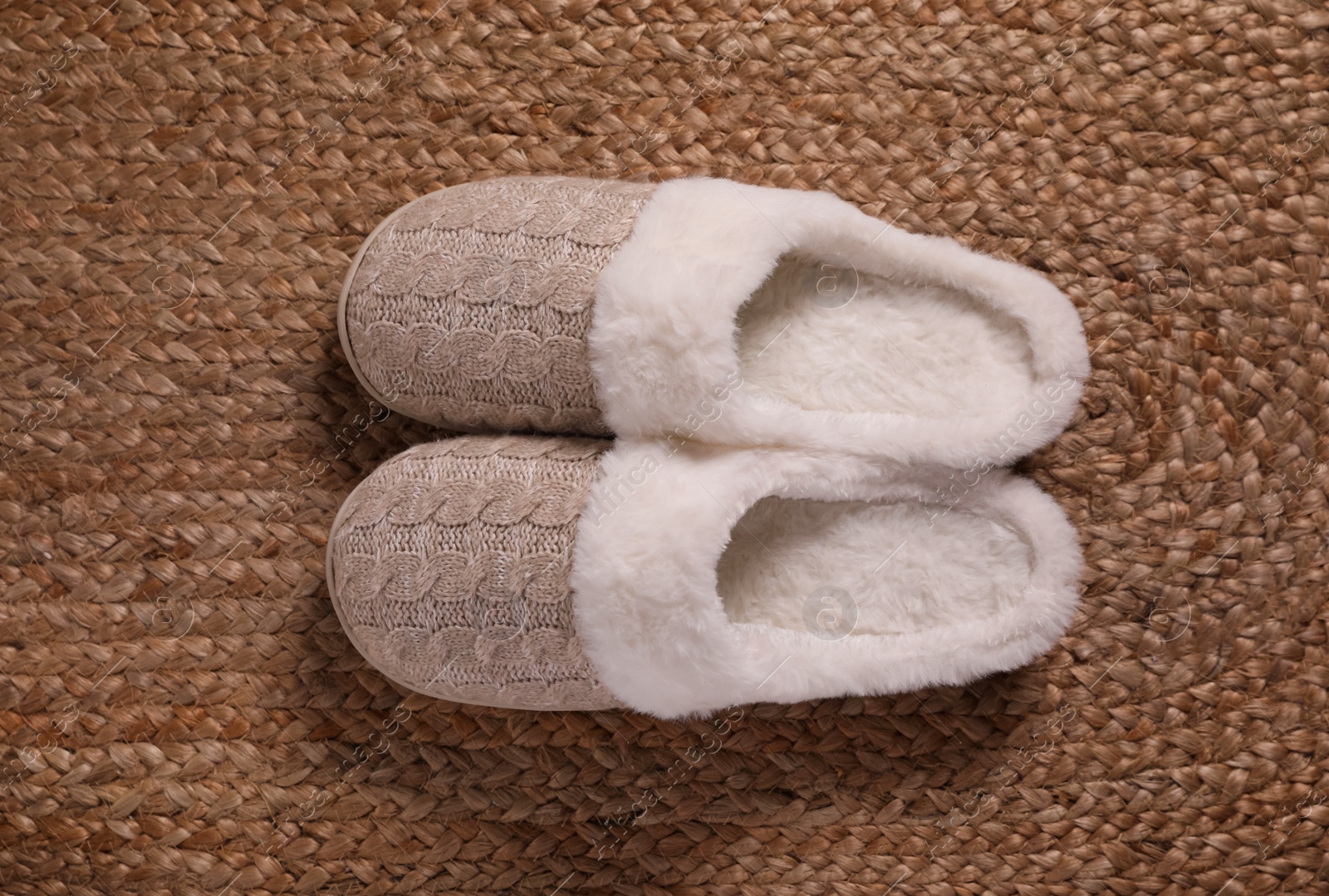 Photo of Pair of warm stylish slippers on wicker carpet, top view