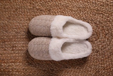 Pair of warm stylish slippers on wicker carpet, top view