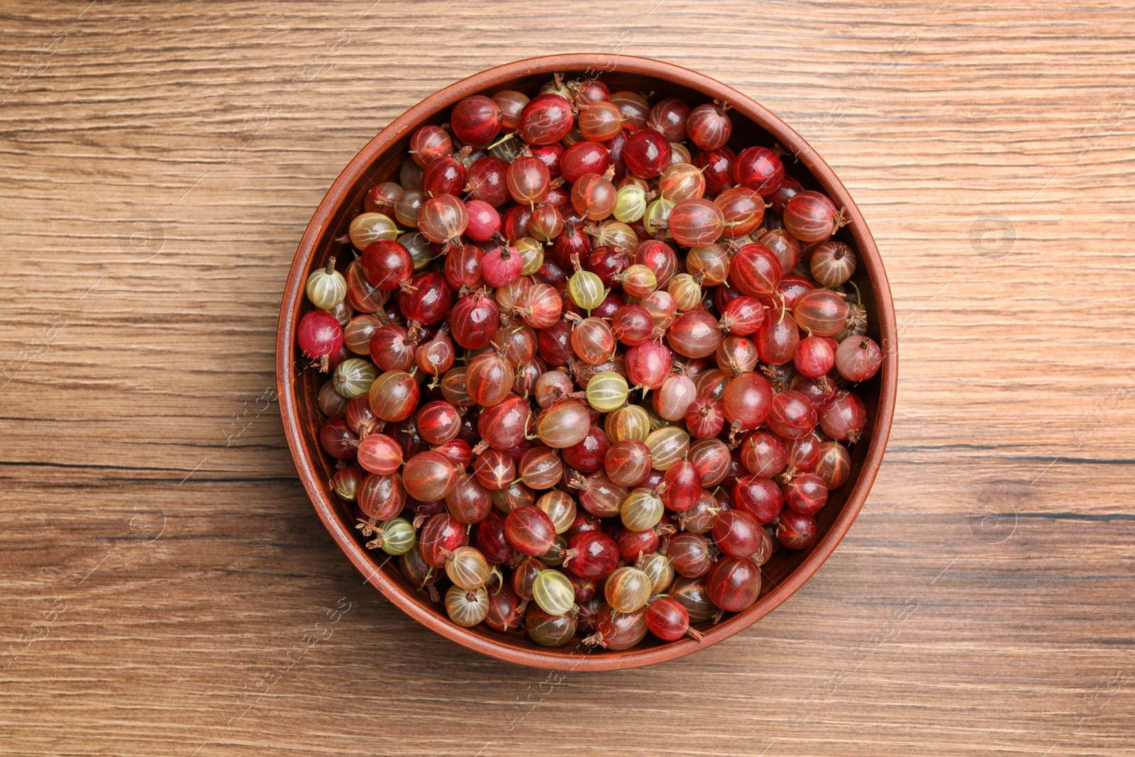 Photo of Bowl full of ripe gooseberries on wooden table, top view