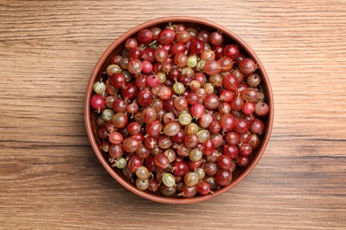 Bowl full of ripe gooseberries on wooden table, top view