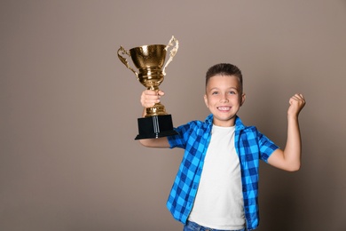 Photo of Happy boy with golden winning cup on beige background