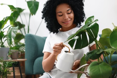 Photo of Happy woman watering beautiful monstera with water indoors. Houseplant care