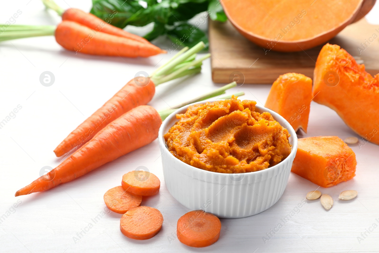 Photo of Bowl with tasty puree, carrots and pumpkin on white wooden table