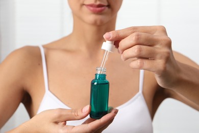 Photo of Woman with bottle of cosmetic serum on blurred background, closeup