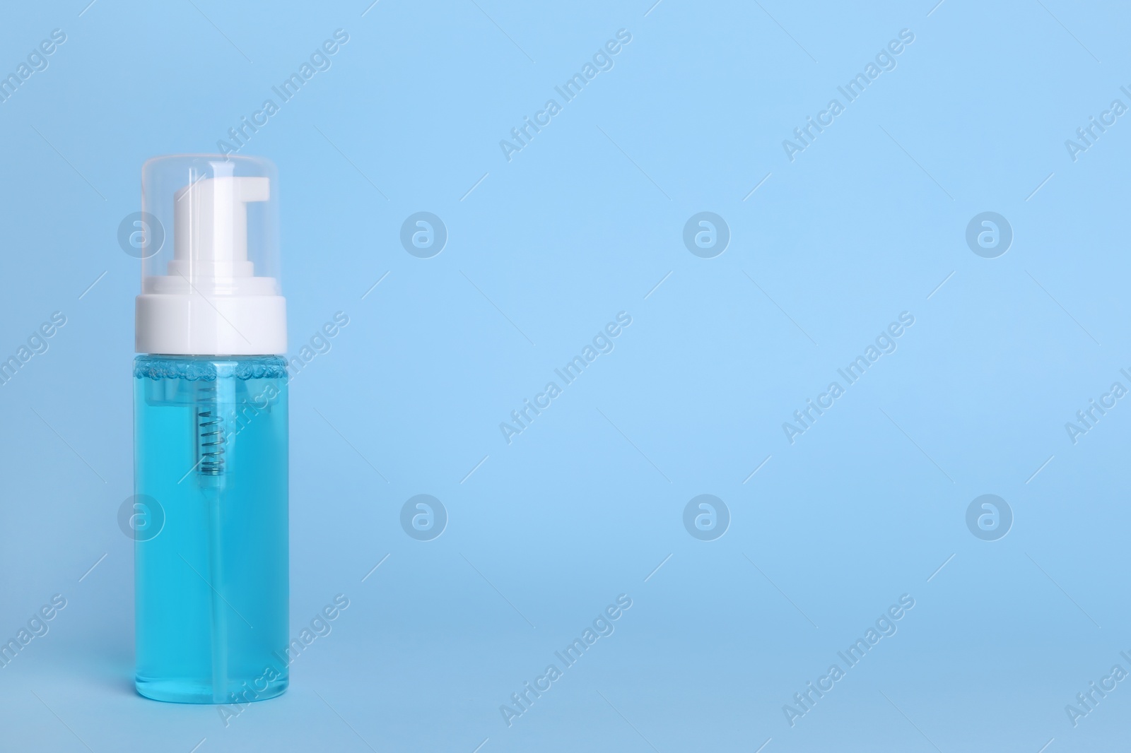 Photo of Bottle of face cleansing product on light blue background. Space for text