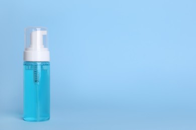 Bottle of face cleansing product on light blue background. Space for text