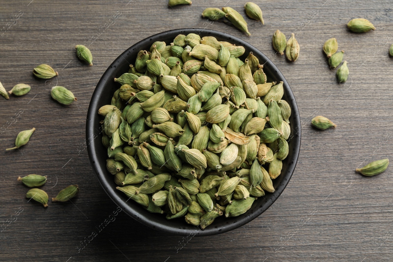 Photo of Bowl of dry cardamom pods on wooden table, top view