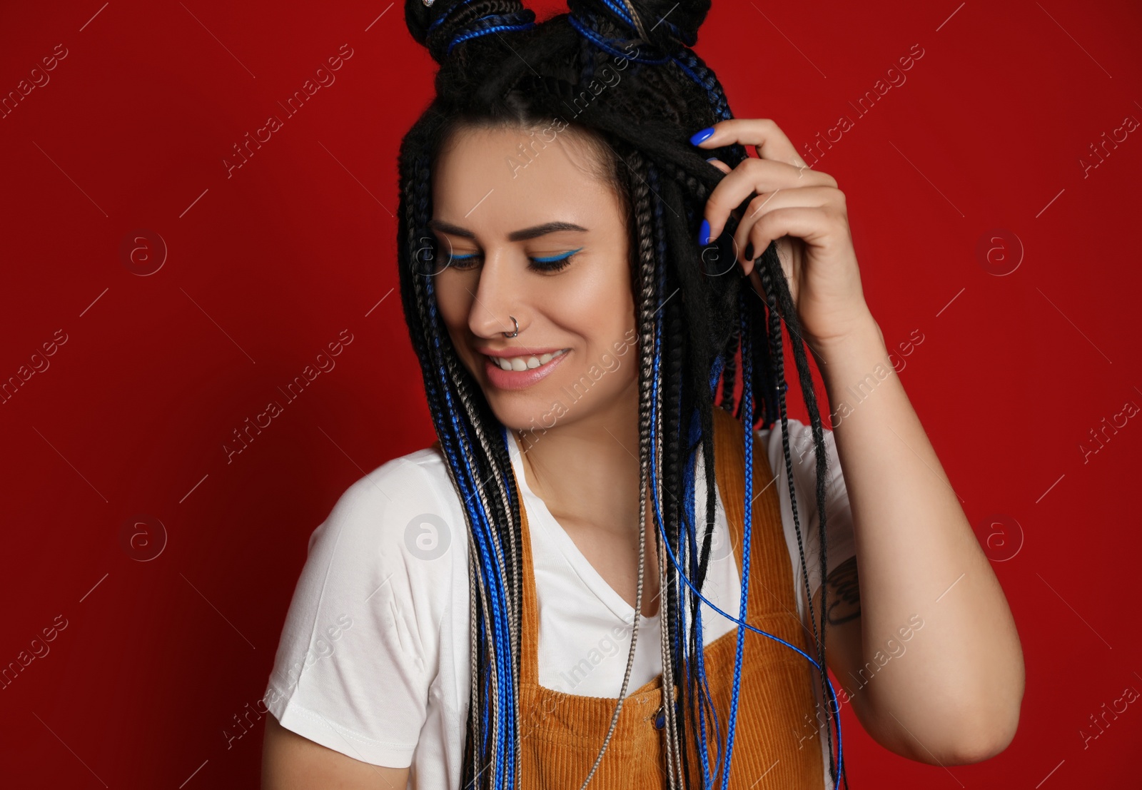 Photo of Beautiful young woman with nose piercing and dreadlocks on red background