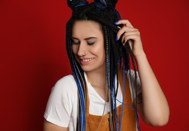 Photo of Beautiful young woman with nose piercing and dreadlocks on red background
